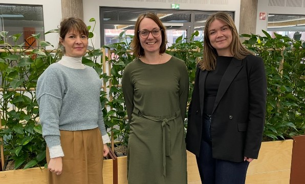 Tre kvinnor framför växtvägg